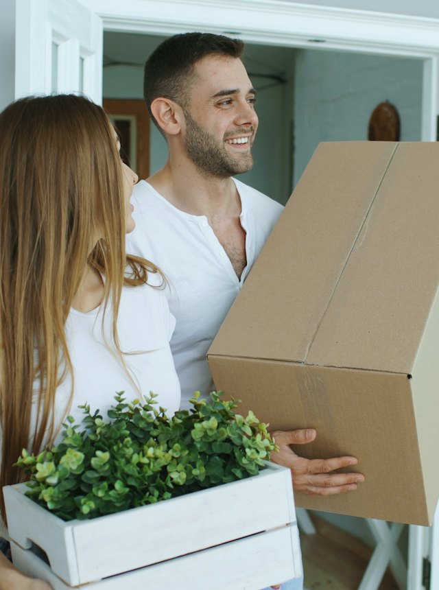 A couple carrying moving boxes into their new home